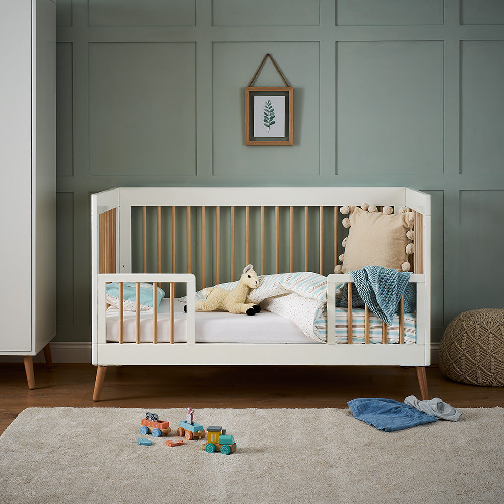 Scandi style cot bed with open rails on all sides, toddler safety rails on the front.